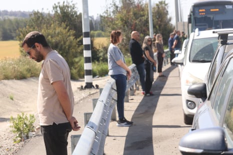 About eight people stood in a line next to their parked cars along a road.