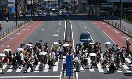 People in Tokyo use umbrellas and parasols to seek relief from the heat while crossing a street outside Shinjuku station.