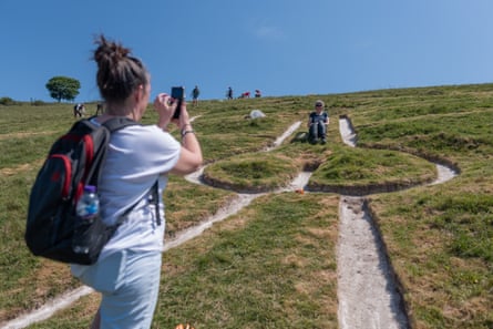 A woman takes a picture of another woman, who is sat down in the groin area of the chalk figure