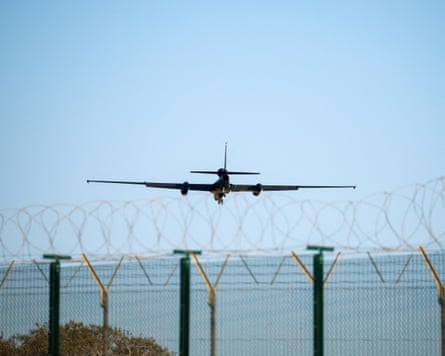 A U-2 aircraft approaches RAF Akrotiri, a plane in blue sky over the sea with barbed wire fence in front