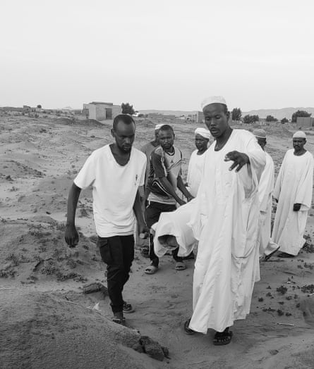 Black and white photo showing a group of men carrying a body wrapped in a shroud on a stretcher across a desert landscape