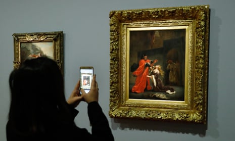 A woman takes a photo of a painting by Delacroix at the Louvre in Paris.