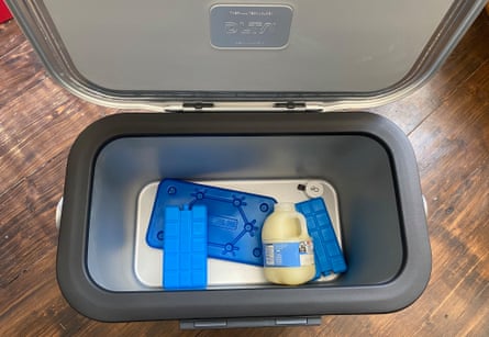 A grey and silver ice box filled with three blue ice packs and one pint bottle of milk
