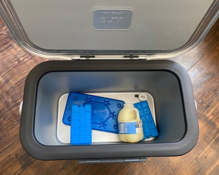 A grey and silver ice box filled with three blue ice packs and one pint bottle of milk