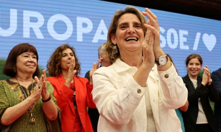 Teresa Ribera applauds as her party celebrates their election victories; other women are seen behind her, also clapping. She is in her mid-50s and has shoulder-length fair hair; she is smiling widely and wears a pale cream top and white cotton jacket