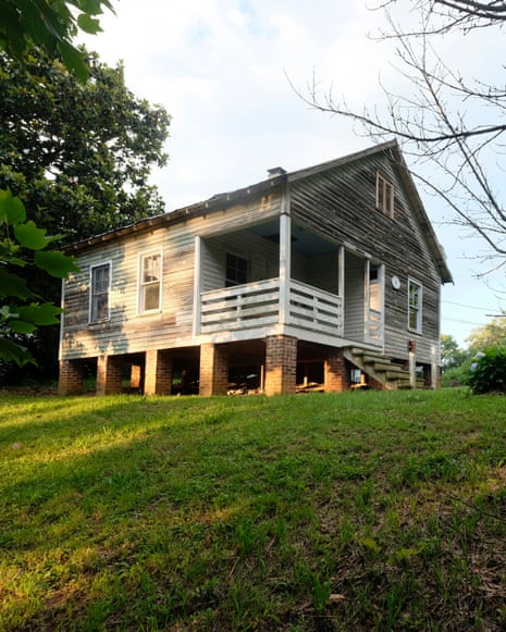 A small wood-framed home in a clearing in the woods.