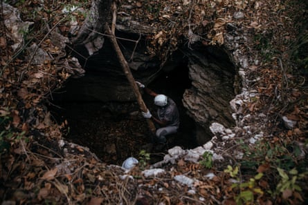 An African man in a hard hat uses a wooden pole to enter a sinkhole-like opening in the ground