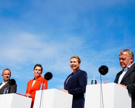 Two men and two women stand at podiums at an outdoors press conference