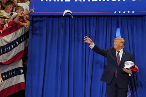 Trump, standing against a blue curtain, frisbeeing a hat toward a crowd.
