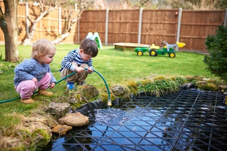 Two small children filling up a pond with a hose