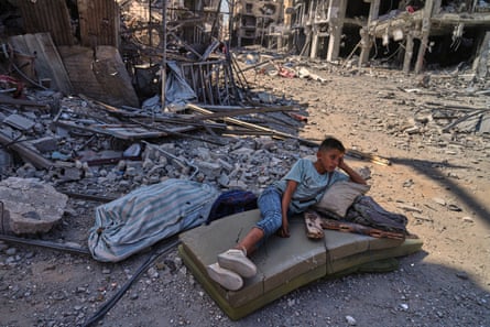 Boy lies on mattresses among the debris of bombed buildings.