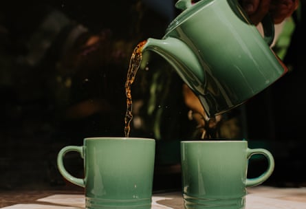 Tea is poured from a green teapot into matching mugs