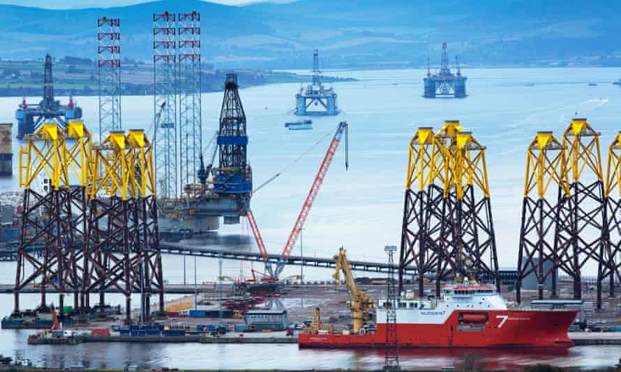 Escena mirando hacia abajo con un barco de casco rojo en primer plano, nuevas torres amarillas y negras en forma de pilón detrás, y en la distancia dos cráteres de petróleo.