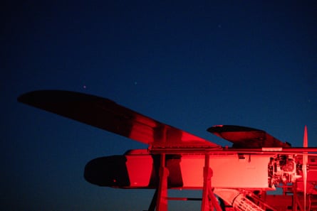 A Ukrainian long-range drone illuminated in red from the side against a blue-black night sky