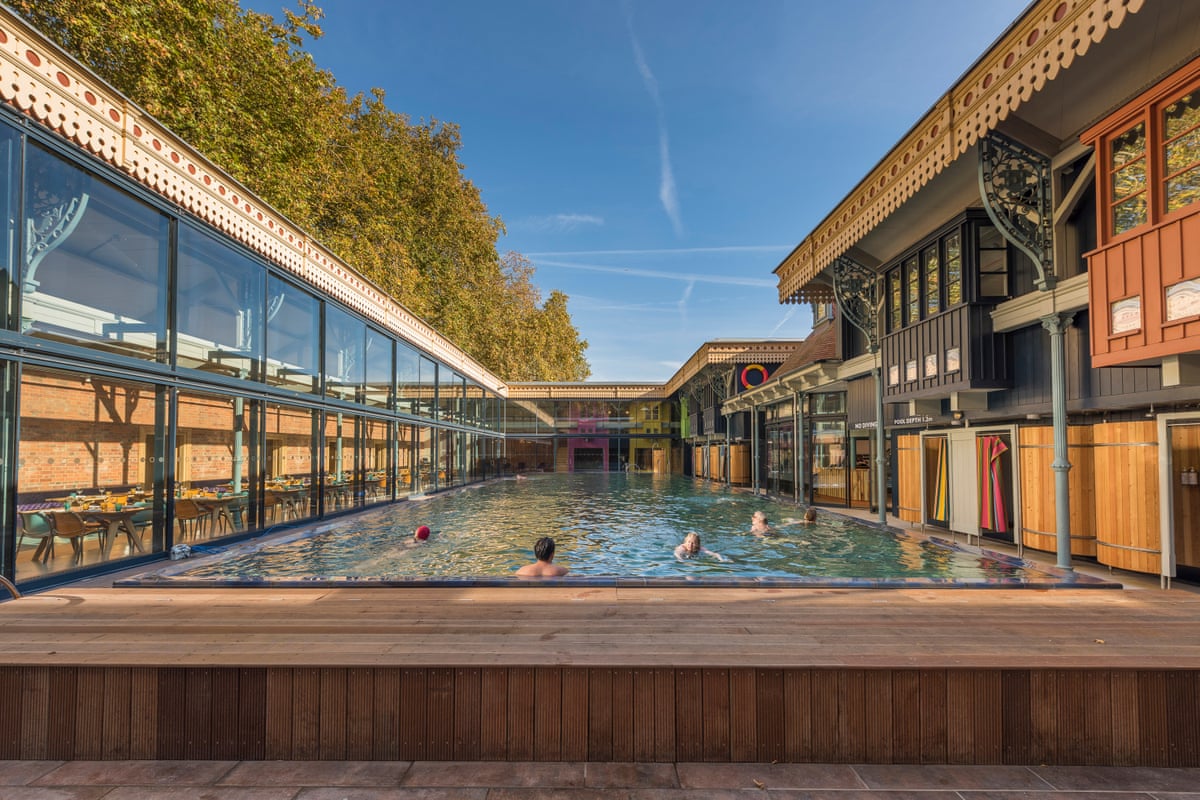 An open-air pool surrounded by glass and wood buildings with a blue sky above