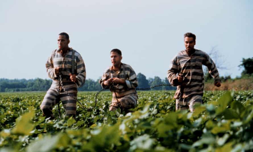 Three men in chains and prison outfits running through a field
