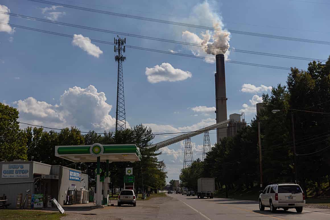 The smokestack from the Gavin power plan billows smoke into a blue sky as a gas station stands in the foreground.