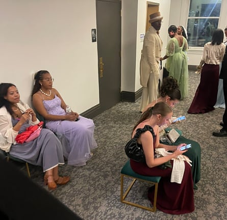 People in ballgowns and tail jackets look at their phones in an office-type room