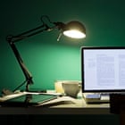 Computer and cell phone illuminated by desk lamp at night
