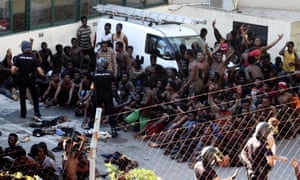 Police officer keep watch over some of the people who managed to jump off the border fence between Spain and Morocco, in Ceuta, on Thursday.