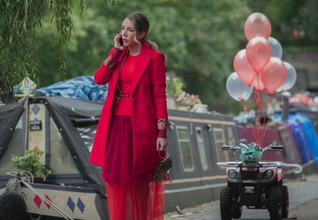 Ryan talks on the phone while she stands on a canal path wearing a bright red jacket and dress.