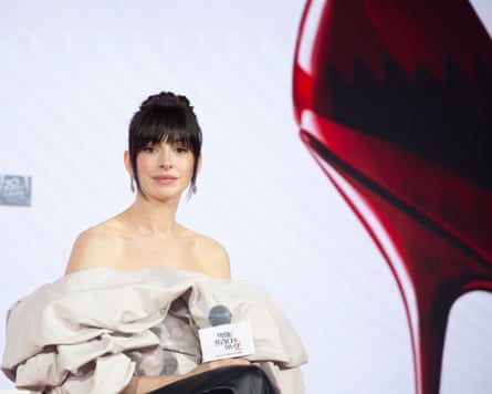 Anne Hathaway seated with part of giant red stiletto on right