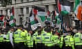 Police form a line outside Whitehall to stop pro-Palestine protesters from spilling onto the road. Protesters are waving the Palestinian flag.