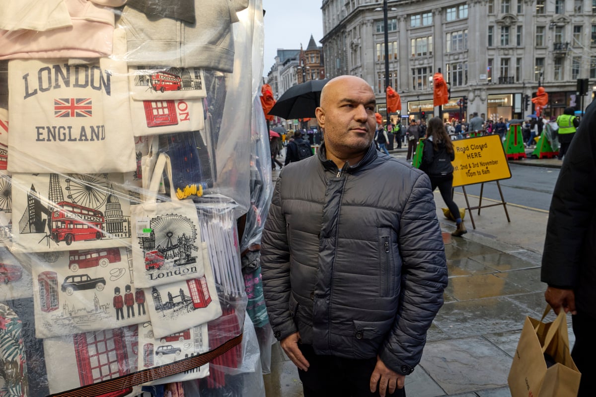 Abbas Shigival stands by his souvenir kiosk, with tote bags depicting London scenes hanging behind him.