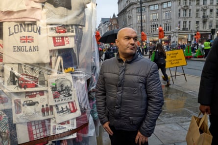 Abbas Shigival stands by his souvenir kiosk, with tote bags depicting London scenes hanging behind him.