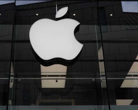 A large white Apple logo is illuminated against a dark background and shadowed windows on the front of a store in Munich.