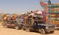 Trucks loaded with people and possessions wait in line