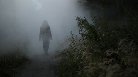 A woman seen from behind on a dark misty path through woodland