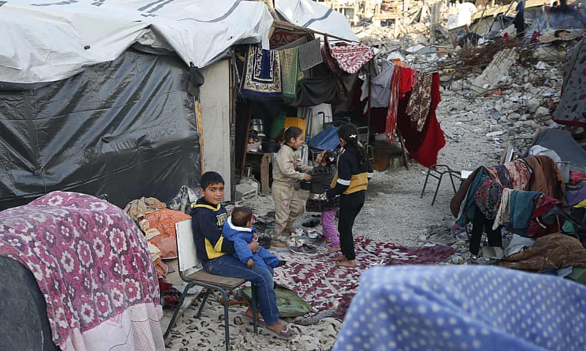 Palestinian children sitting on seats between shelters put up amid the rubble