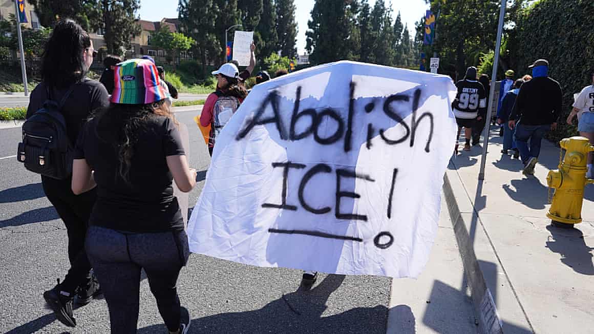 Protesters hold up a white banner with the words 'Abolish Ice' on it
