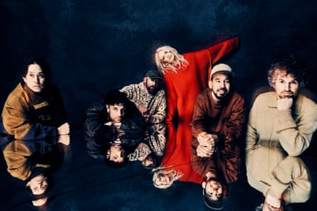 five men leaning on a reflective surface and a woman in a red jumper with her arm extended