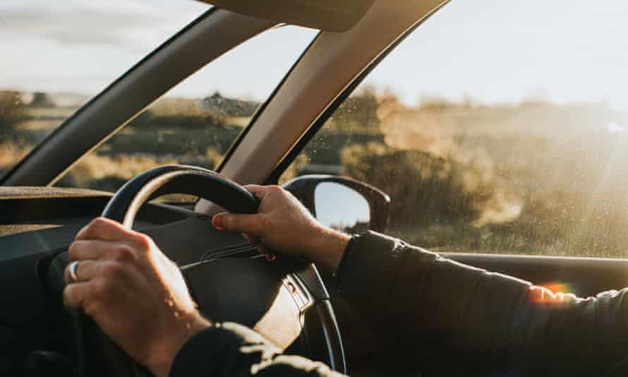Hand holds a black steering wheel. Car is illuminated by low, warm sun at dusk.