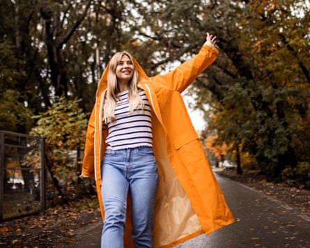 Woman walking through a tree-lined street during autumn while wearing an orange raincoat