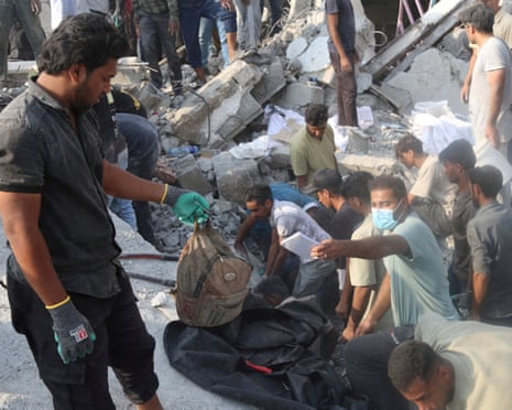 people looking through rubble, one man hands another a child's school bag