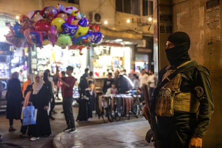 A member of the Syrian security forces stands guard as people shop at a market