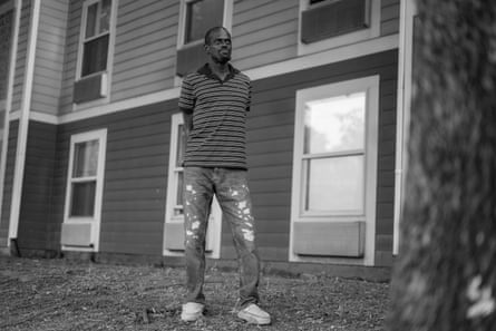 A man in a striped polo shirt and jeans stands outside a house