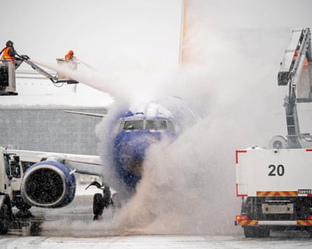 Crew on a cherry picker sprays great cloud of white fog at an airplane.