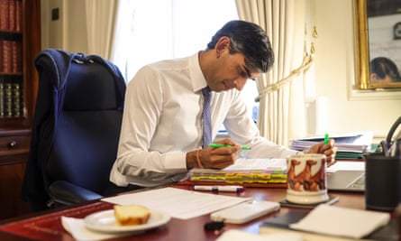 Rishi Sunak holds a pen as he looks at documents, with a labrador-design mug beside him on his desk