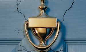 Cracks appear in a front door behind a brass knocker.