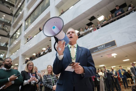 Man in suit speaks into bullhorn in large interior building.