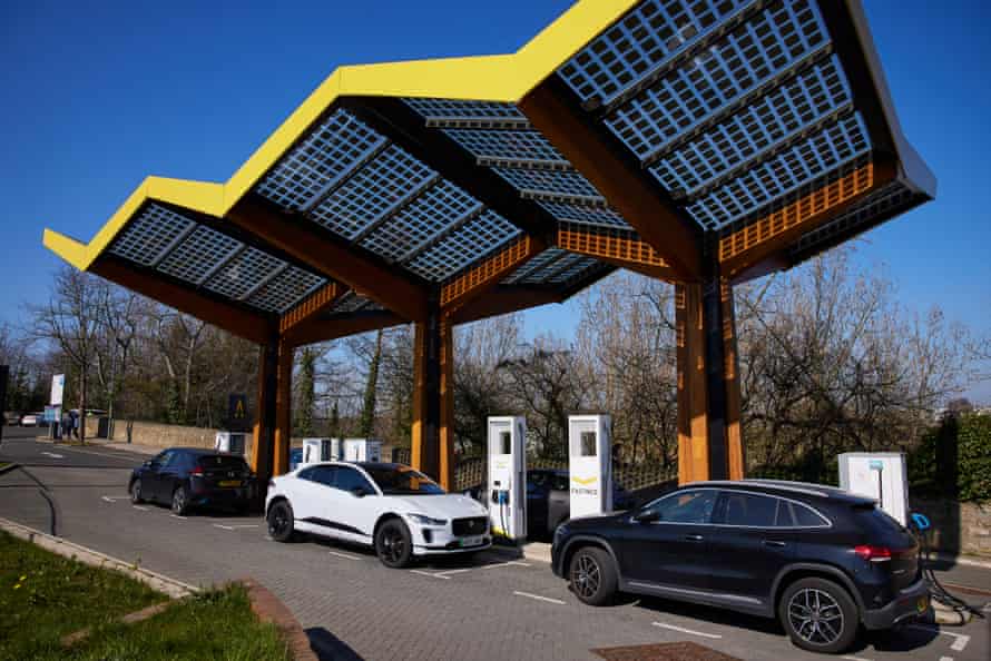 Three electric cars charging at a roadside station with a beautiful yellow zigzag canopy protecting the chargers
