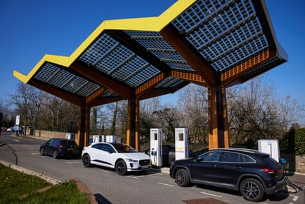 Three electric cars charging at a roadside station with an attractive yellow zig-zag canopy sheltering the chargers