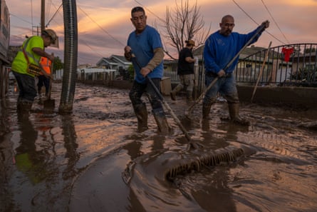 I residenti lavorano per respingere il fango umido che ha intrappolato i veicoli e ha invaso diverse case l'11 gennaio 2023 nella piccola città non incorporata di Piru, a est di Fillmore, in California.