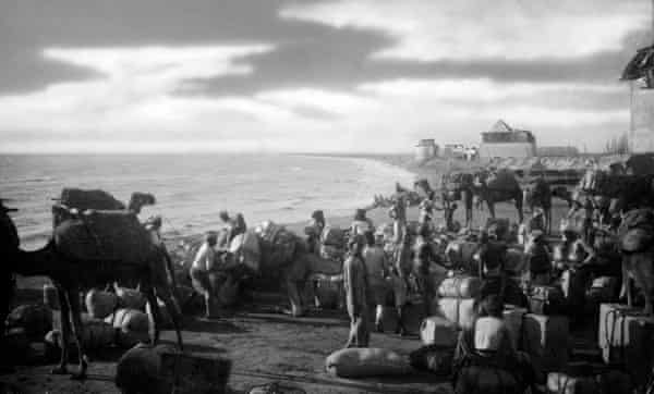Traders on a beach with camels and sacks of coffee beans