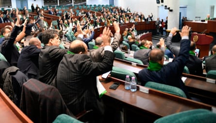 Lawmakers, wearing scarves in the colours of the national flag, hold up their hands to vote in the national assembly