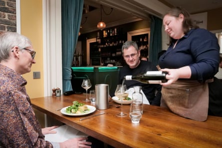 Waitress pouring wine while Lian and Carl look on